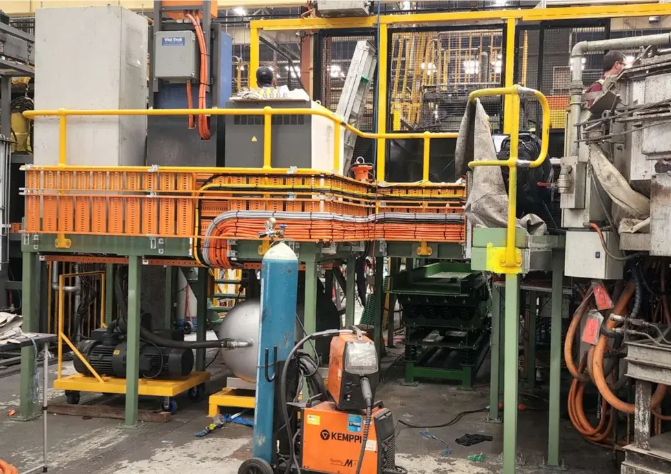 Steel access platform with yellow handrails fitted among existing industrial machinery, cable trays and mesh guarding