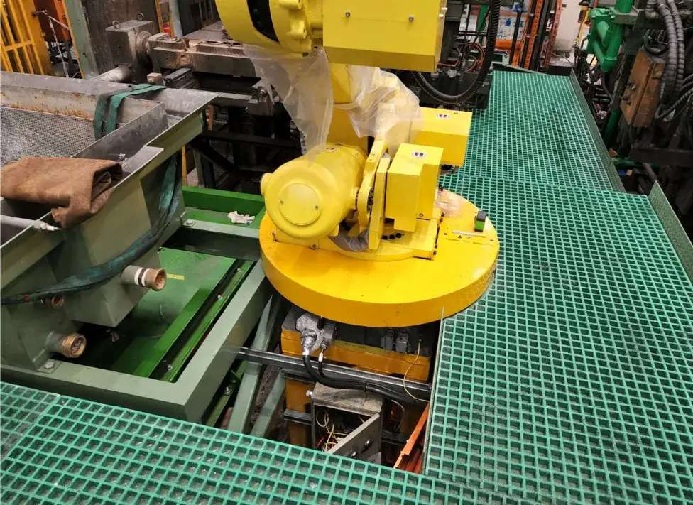 Green grated platform fitted around the base of a yellow industrial robot and adjacent machinery