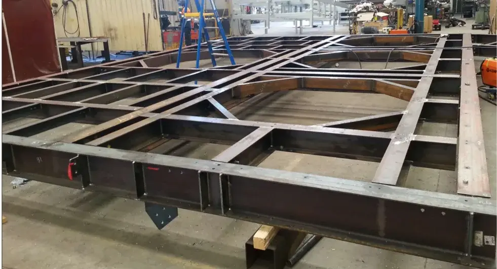 Structural steel platform frame with cross members and connection plates laid out in a fabrication workshop
